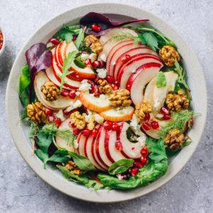 Healthy multi greens salad plate with apple, walnut, pomegranate, cheese, dressing on light background. Healthy food. Clean eating.